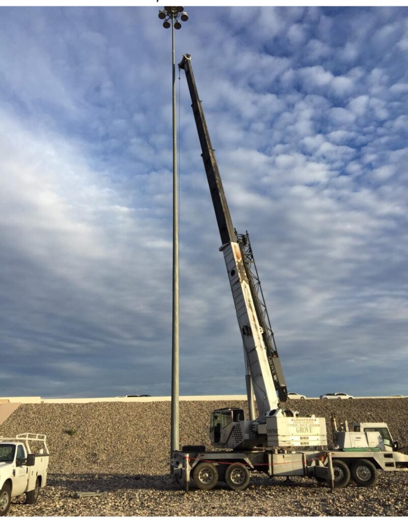A crane from Langford Crane Service, Inc., lifting a technician toward a tall light pole against a cloudy sky, demonstrating maintenance work using a 50-ton crane rental in Las Vegas.